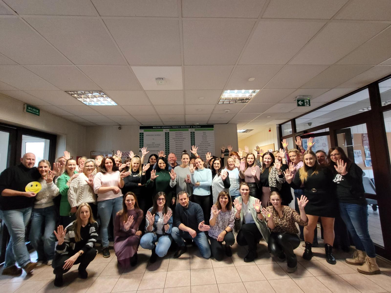 Grupa pracowników MOPR uśmiecha się i pokazuje symbol Dnia Adopcji namalowaną buzię na dłoni
